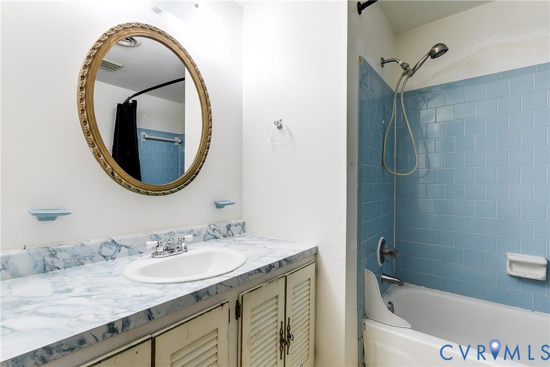 White vanity with louvered cabinet doors, oval undermount sink, and patterned countertop