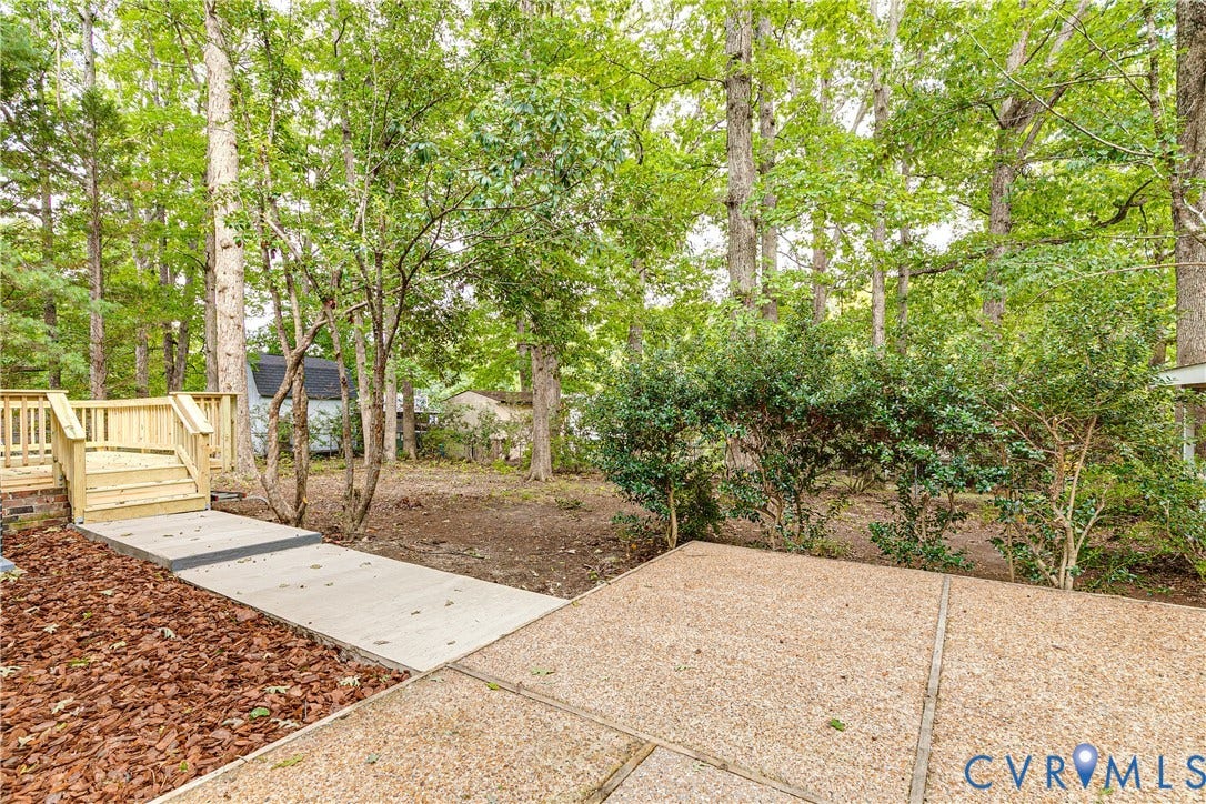 Expansive backyard featuring a new wood deck, concrete patio, concrete walkway, and mature trees