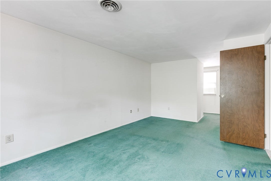 White painted walls with green carpet flooring and a wood-finish interior door