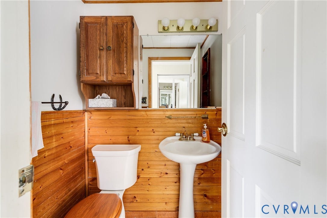 Pedestal sink, wood-paneled walls, wall-mounted wood cabinetry, vanity mirror, and white paneled door