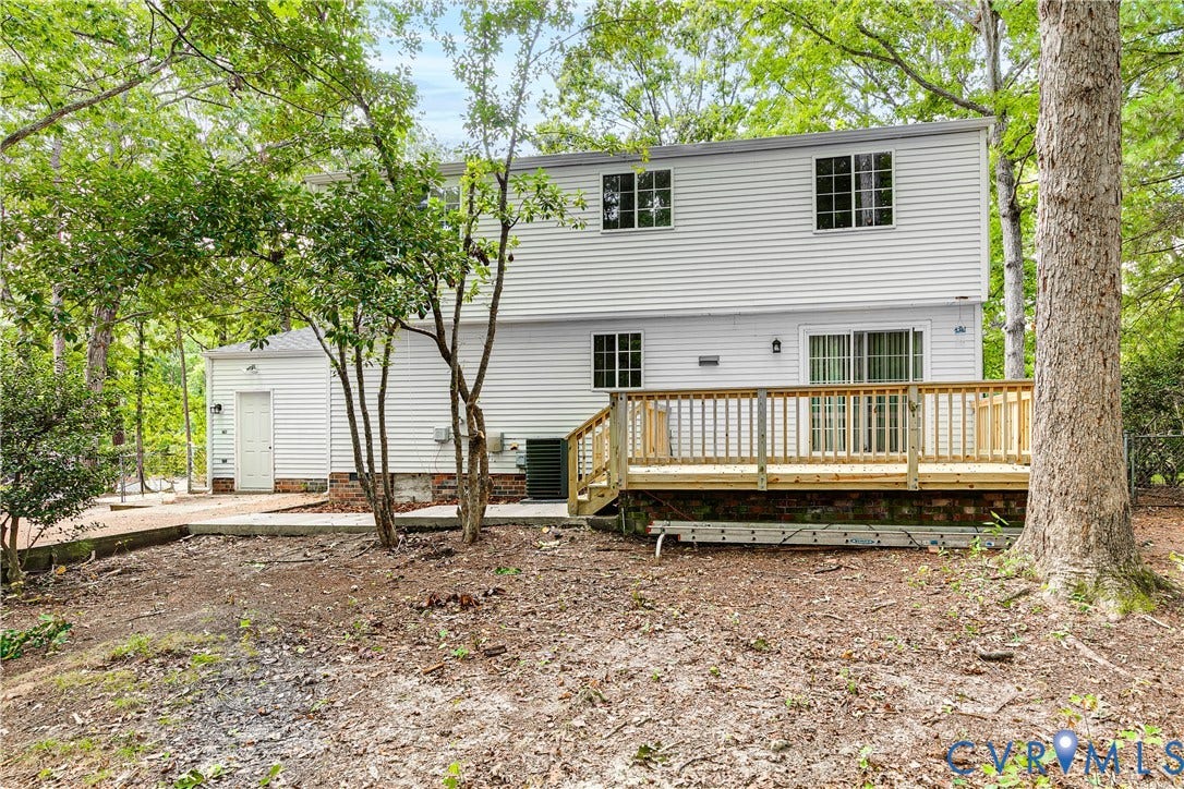 Rear exterior featuring white horizontal siding, a wooden deck with railing, and a sliding glass door
