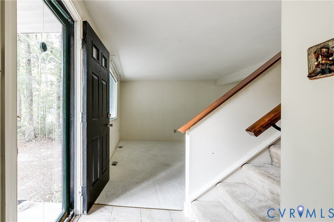 Entryway featuring a paneled door, tiled flooring, carpeted stairs, and a wood handrail