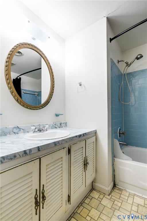 Bathroom featuring a vanity with louvered cabinet doors, a drop-in sink, and a framed mirror