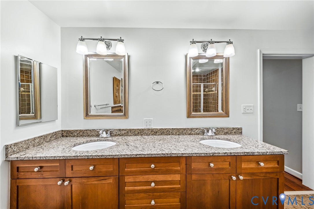 4820 Old Main Street, #503, Sky Line Condo, Richmond, VA 23231 Dual vanity with integrated sinks, granite-finish countertop, wood-finish cabinetry, and framed mirrors with overhead lighting