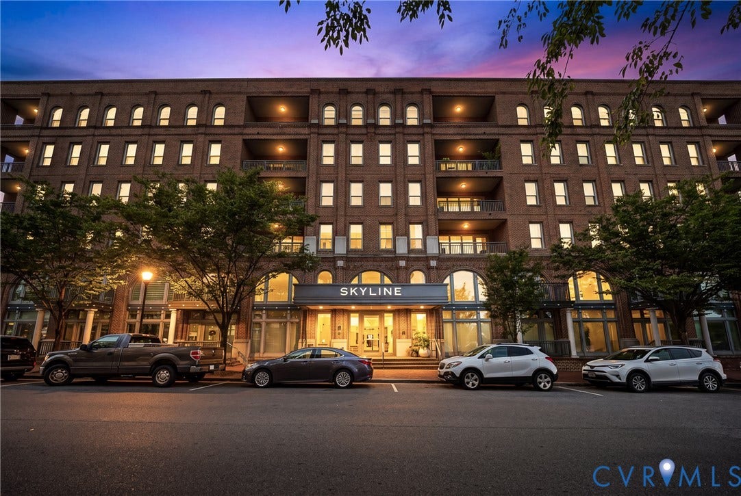 4820 Old Main Street, #503, Sky Line Condo, Richmond, VA 23231 Multi-story brick building with arched windows, prominent street-level entrance, recessed balconies, and integrated exterior lighting