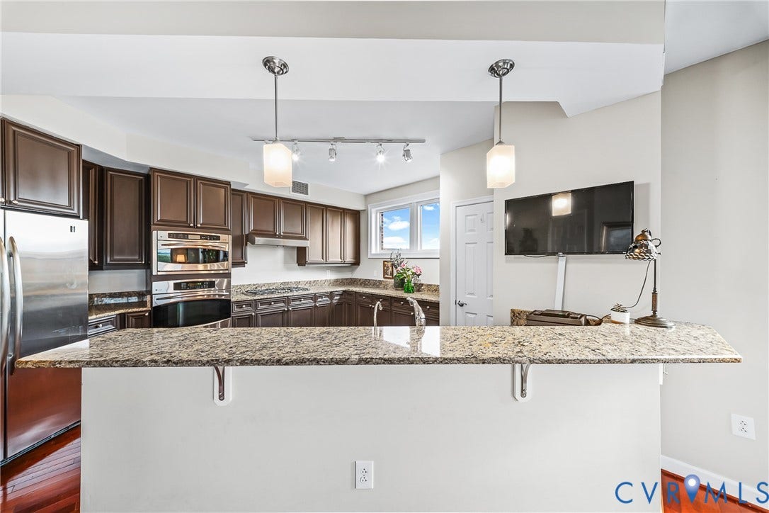 4820 Old Main Street, #503, Sky Line Condo, Richmond, VA 23231 Open-concept kitchen featuring dark wood cabinetry, stainless steel appliances, granite-style countertops, and pendant lighting