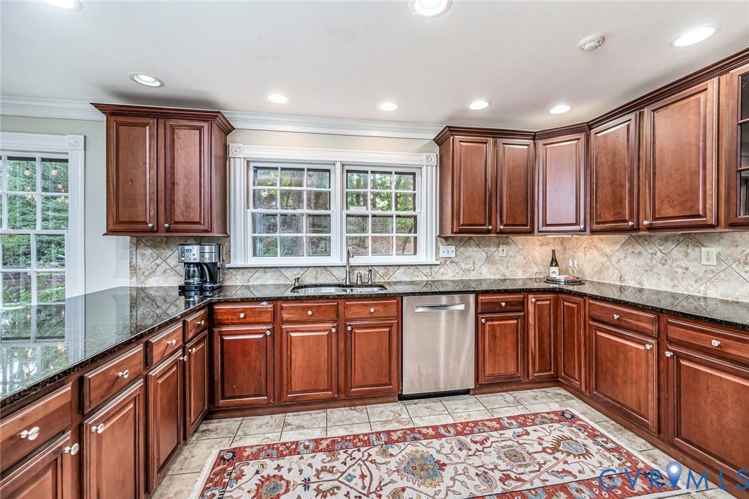 Kitchen featuring wood cabinetry, granite  countertops, tiled backsplash, and stainless steel dishwasher