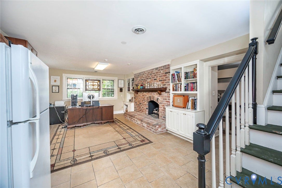 Brick fireplace with a wood mantle, built-in shelving, wood-frame windows, and tile flooring