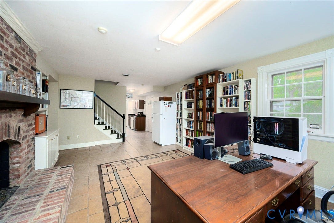 Brick fireplace with a wood mantle, built-in shelving, tile flooring, and a window with grid panes