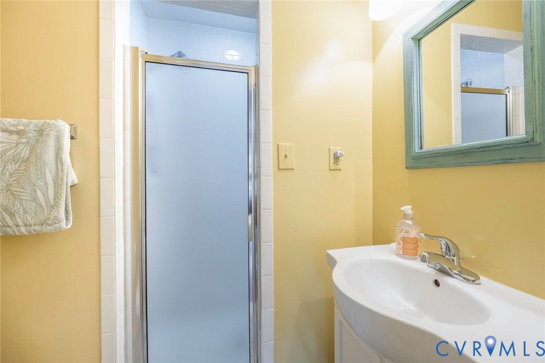 Vanity with integrated basin, single-handle faucet, wall-mounted mirror, and enclosed shower with frosted glass door
