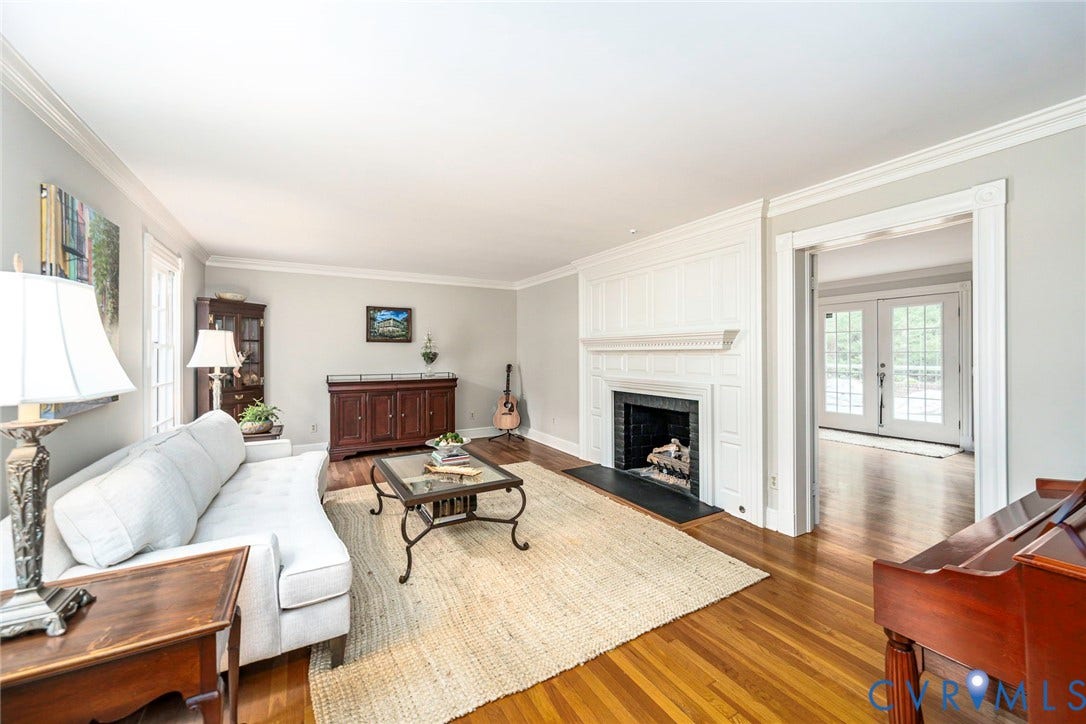 Hardwood flooring, crown molding, a fireplace with a white mantel, and an arched doorway with French doors