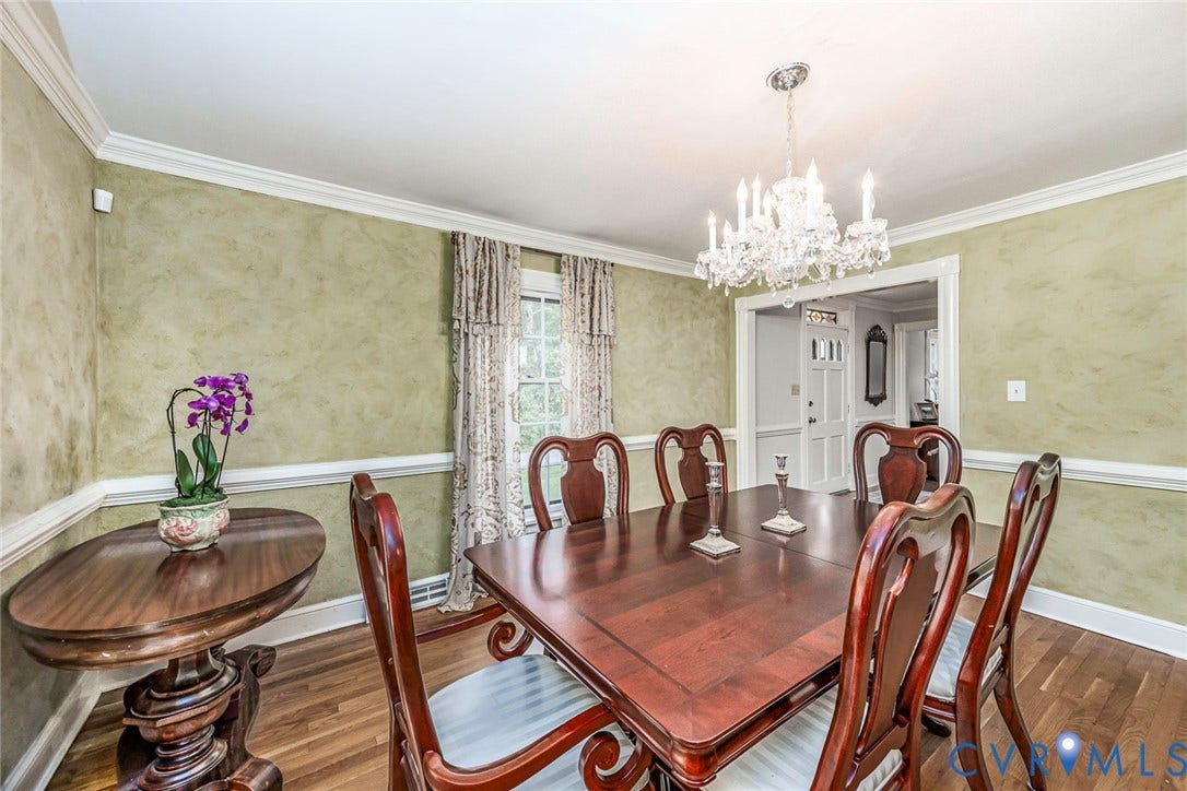 Hardwood flooring, decorative wall finish, crown molding, chair rail, and an elegant chandelier