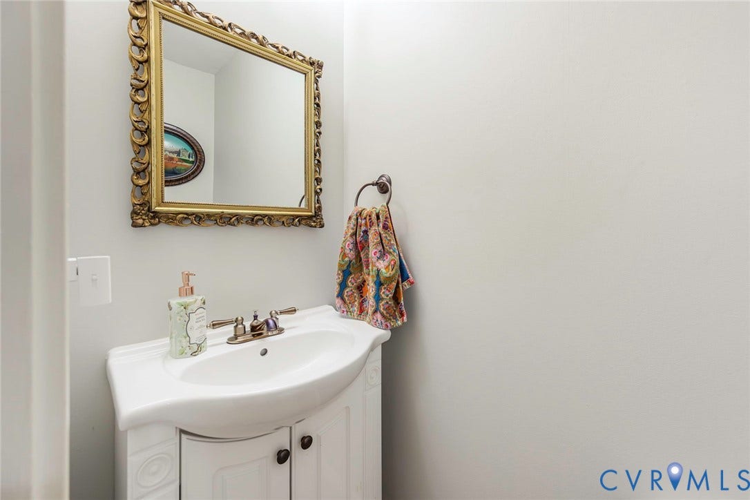 White vanity with a single basin sink, dual-handle faucet, and an ornate framed mirror