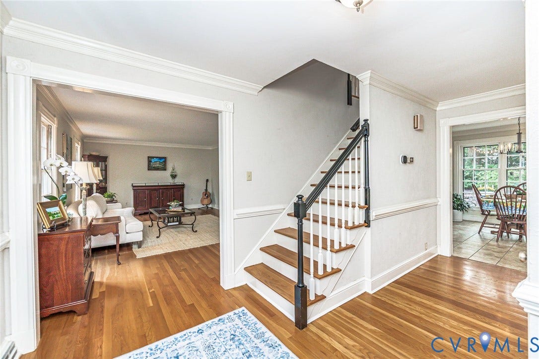 Hardwood flooring throughout the entry, staircase with white risers and dark wood handrail, and crown molding