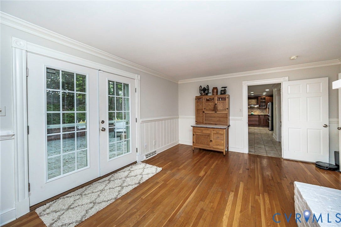 Wood-finish flooring, white paneled French doors, crown molding, white wainscoting, and a doorway to a kitchen with tile flooring