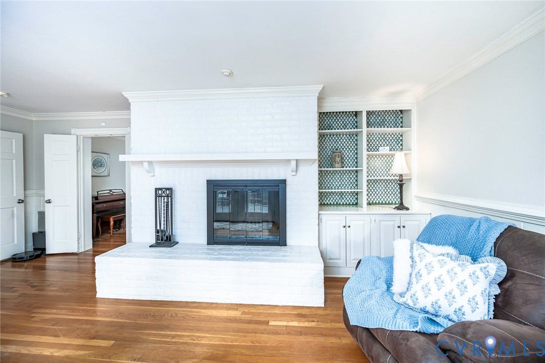 Hardwood flooring, brick fireplace with mantel, built-in shelving, built-in lower cabinetry, and crown molding