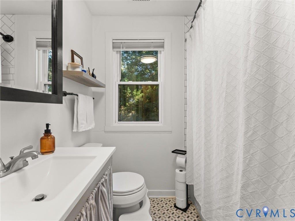 3933 Alma Avenue, Richmond, VA 23222 White subway tile shower surround, window with white trim, engineered wood vanity, and patterned floor tile