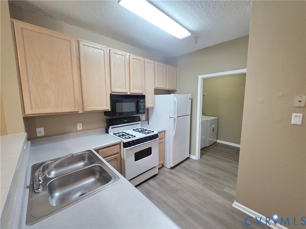 Kitchen with wood-finish cabinetry, a double basin stainless steel sink, and light-toned countertops