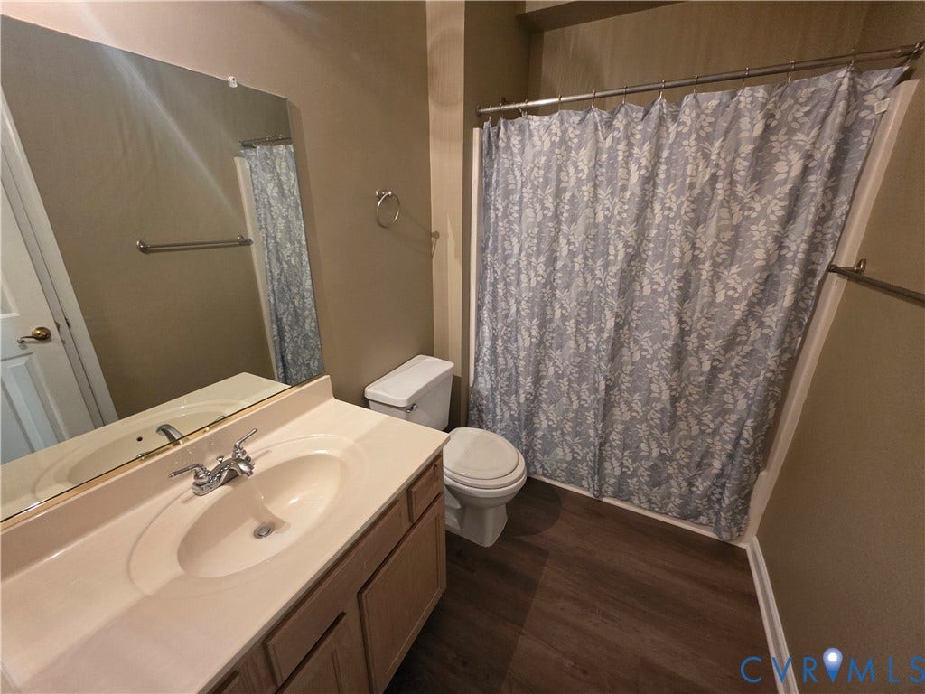 Bathroom featuring a neutral-toned vanity with an integrated sink, polished chrome faucet, full-width wall mirror, and wood-finish flooring