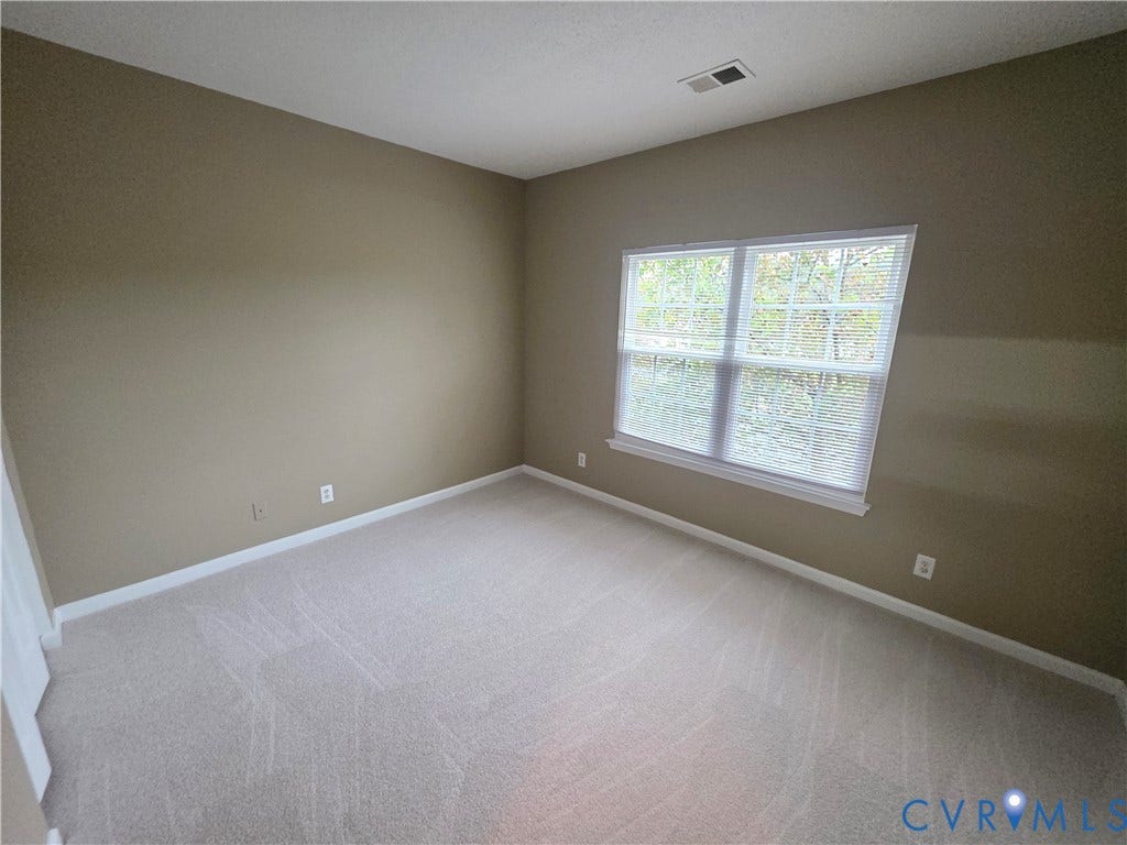 Neutral-toned walls, light-colored carpeting, and a double window with blinds