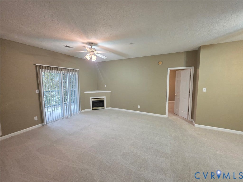 Recessed corner fireplace, sliding glass door, overhead ceiling fan with light fixture, light-toned carpeting, and neutral wall paint