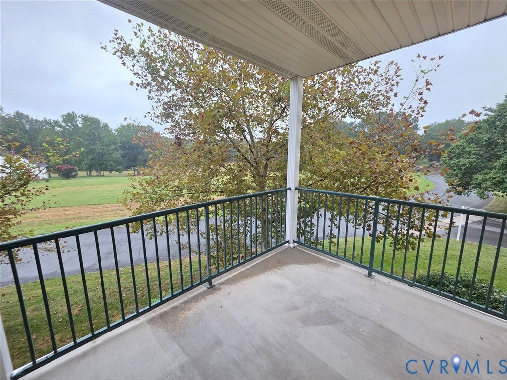 Balcony with concrete flooring and dark metal railings, featuring a white support column and slatted ceiling