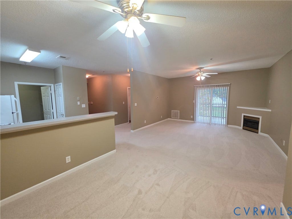 Expansive carpeted living area with a built-in fireplace, sliding glass door, and two ceiling fans