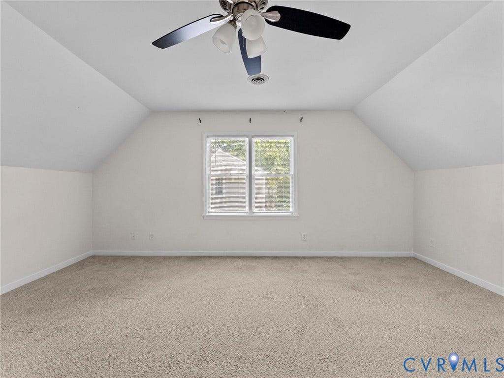 Vaulted ceiling, ceiling fan with integrated lighting, neutral-toned carpeting, and a double-hung window
