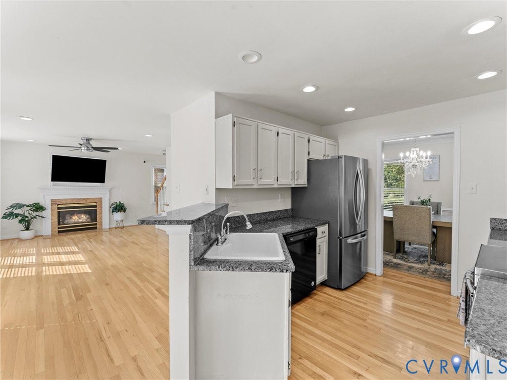 Hardwood flooring, kitchen with granite countertops, stainless steel refrigerator, white cabinetry, and a fireplace in the living area