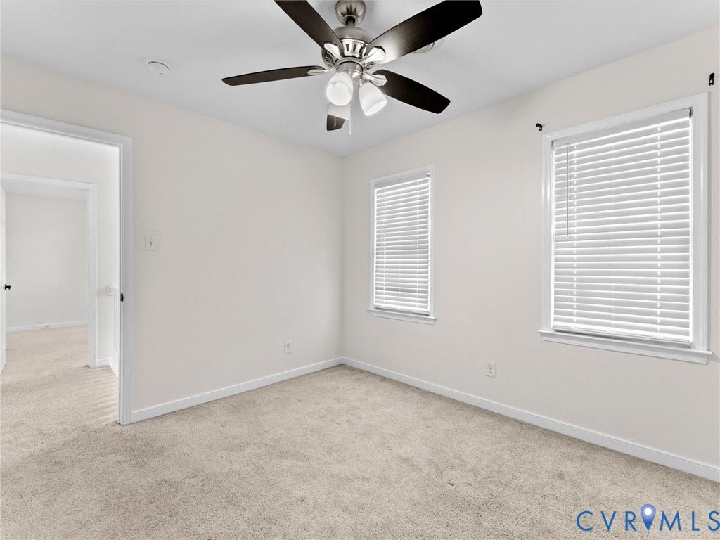 Neutral wall tones, carpeted flooring, two windows with blinds, and a ceiling fan with integrated lighting