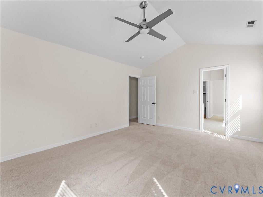 Vaulted ceiling with a brushed nickel ceiling fan, neutral wall paint, and light-toned carpet flooring