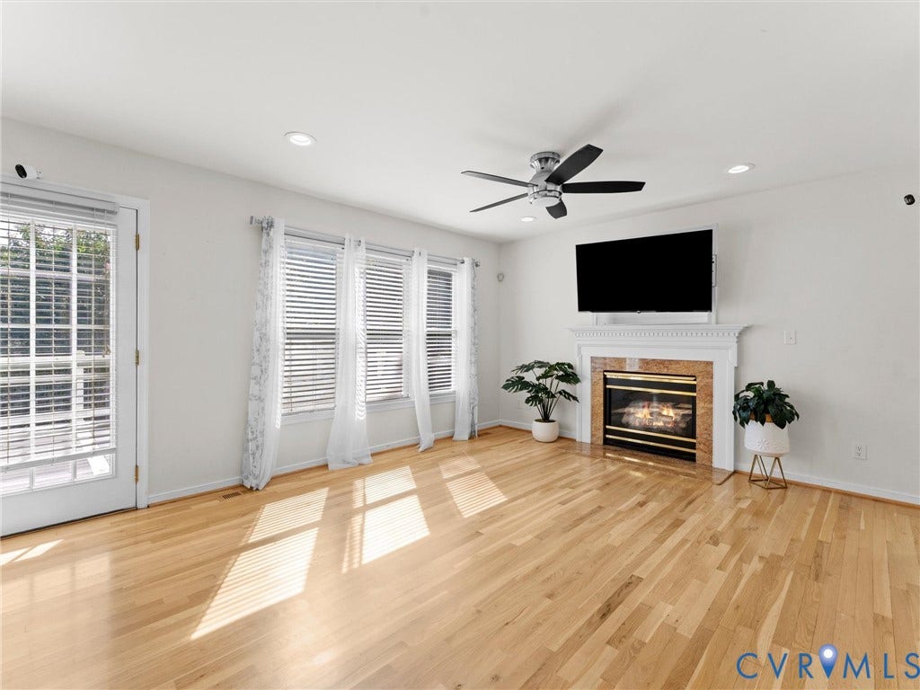 Light wood-finish flooring, recessed ceiling lighting, ceiling fan, fireplace with detailed mantel, and multiple windows