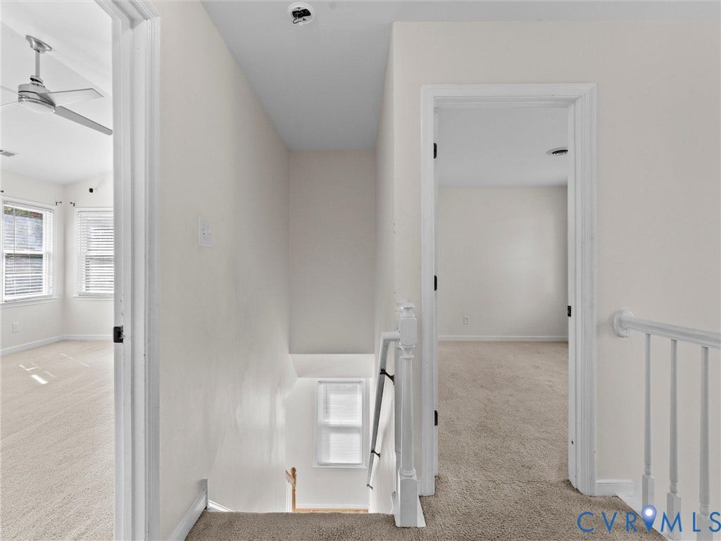 Carpeted hallway with painted balusters and railings, leading to rooms with ceiling fans and multiple windows