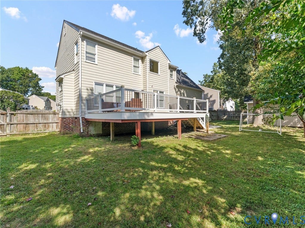 Expansive backyard featuring a wood deck with railings, mature trees, and a wooden fence