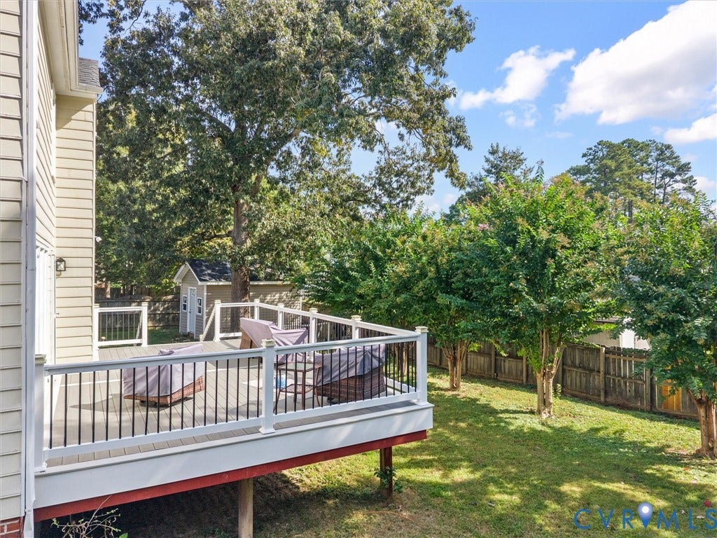 Spacious outdoor deck with white railings and dark balusters, overlooking a fenced backyard with mature trees