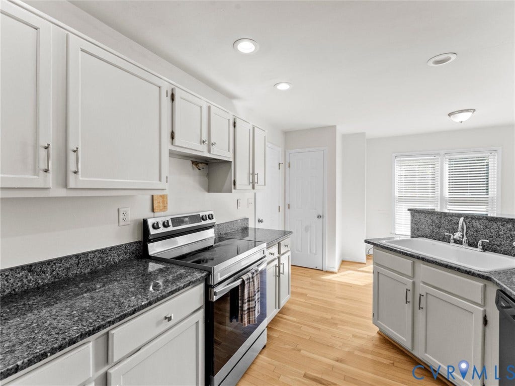 Kitchen featuring light wood-finish flooring, white cabinetry with silver-tone hardware, dark speckled countertops, and recessed ceiling lighting