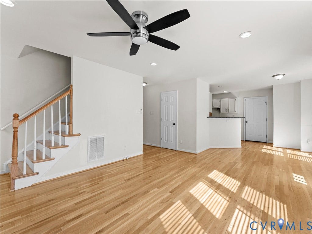 Light wood-finish flooring, staircase with wood handrail and white balusters, contemporary ceiling fan, recessed lighting, and white paneled doors