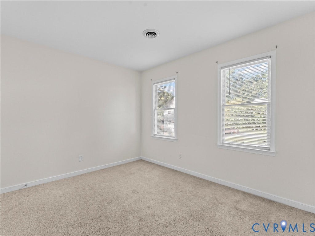 Neutral wall paint, plush carpet flooring, and two windows with blinds