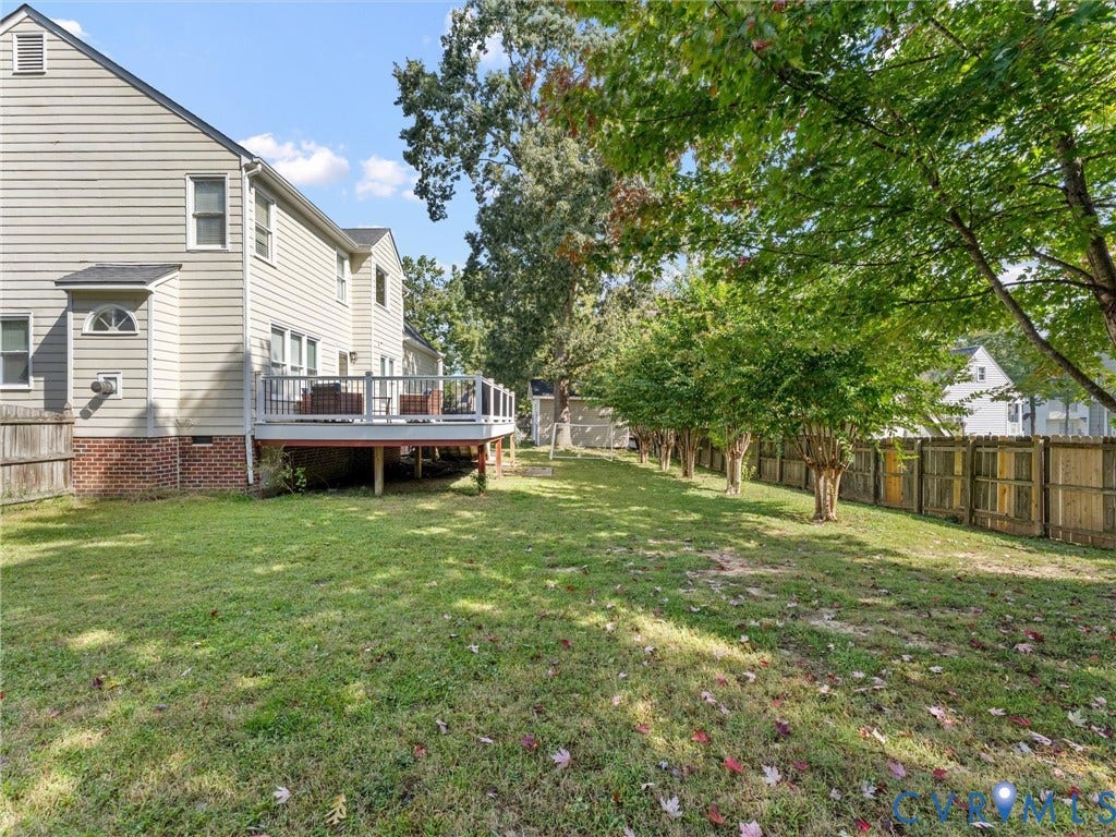 Expansive grassy yard featuring a wood privacy fence, mature trees, and a raised wood deck