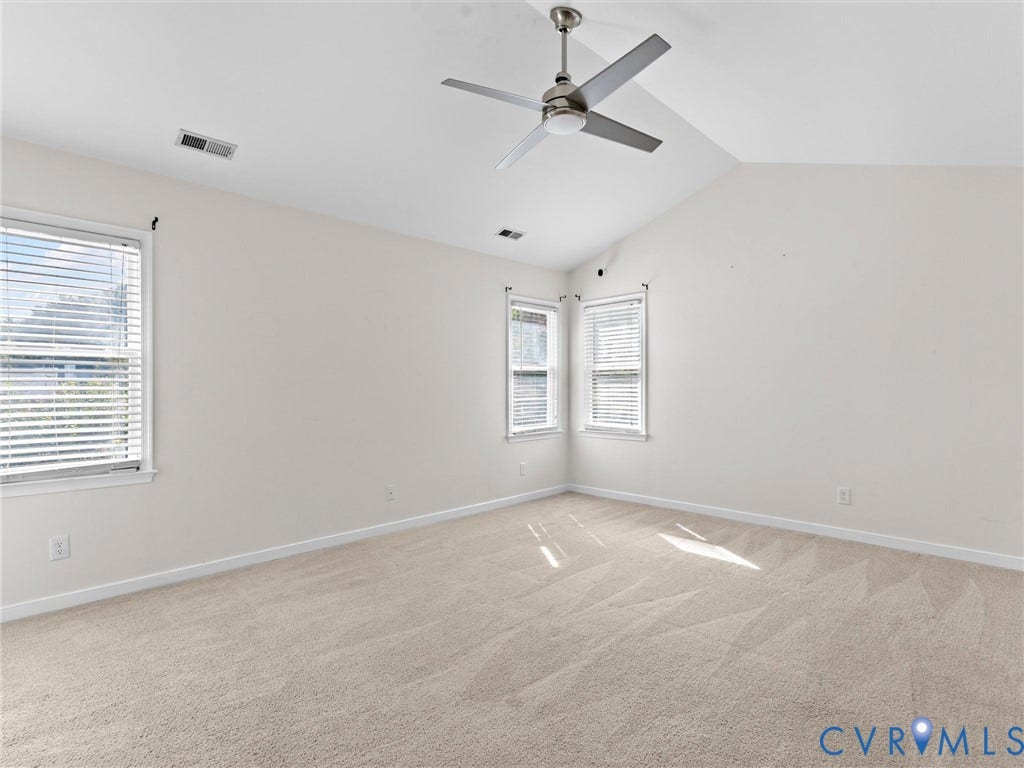 Vaulted ceiling, two windows with blinds, light-colored carpet, and a ceiling fan with brushed nickel finish