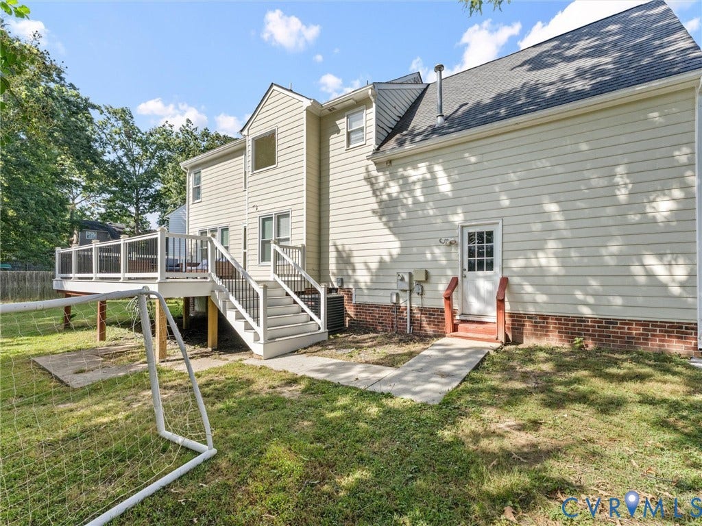 Rear exterior featuring a spacious elevated deck with white railings, a multi-level staircase, and a walk-out basement door with an exterior landing