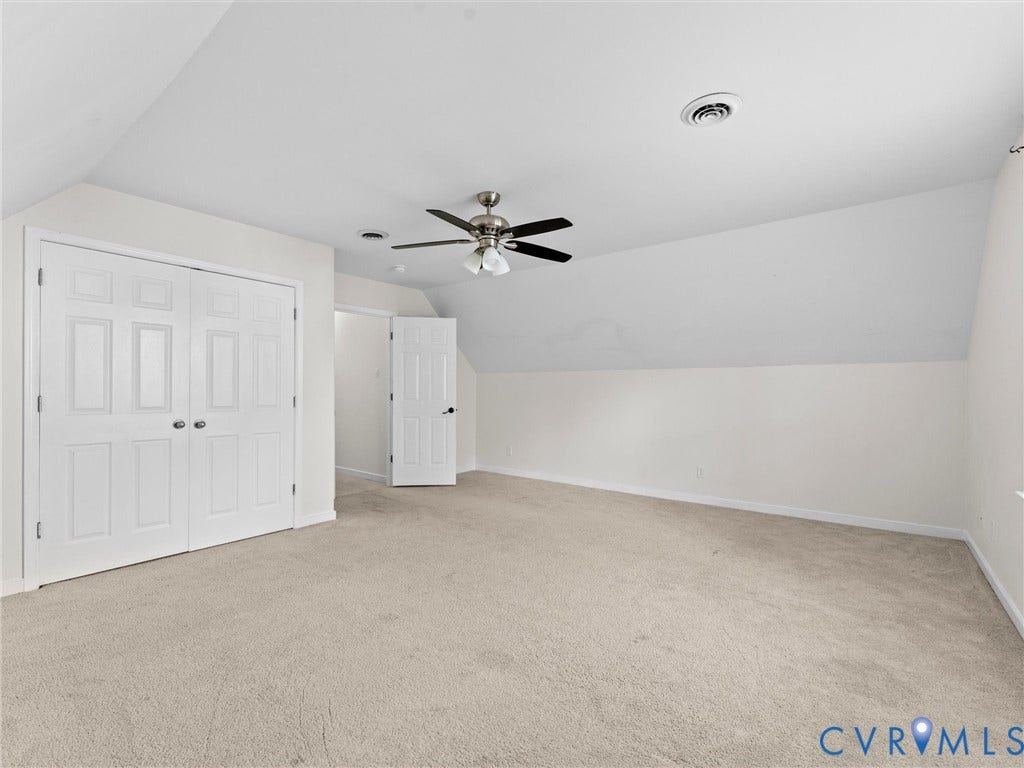 Expansive carpeted room featuring a ceiling fan, white paneled doors, and a sloped ceiling