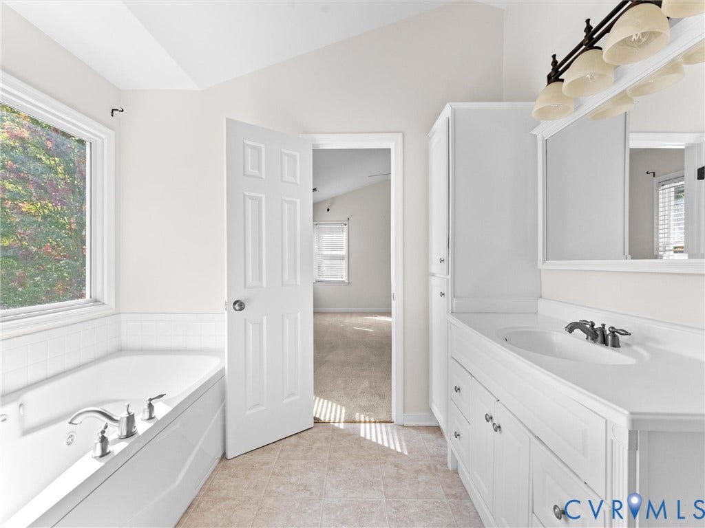 Tile flooring featuring a built-in soaking tub with chrome fixtures, a single vanity with an integrated sink, and white cabinetry with brushed nickel hardware