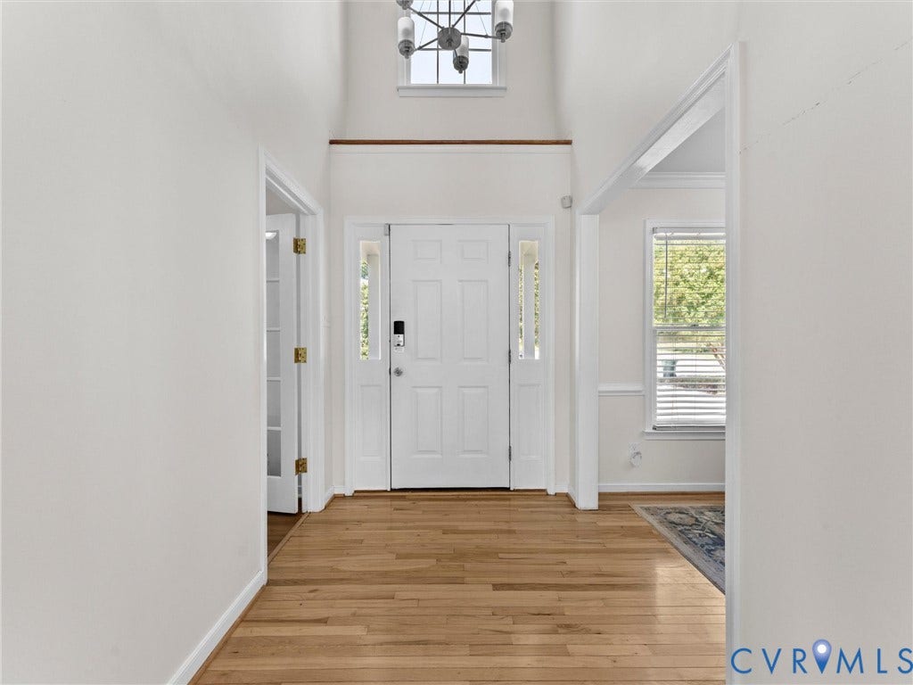 Vaulted entry foyer with wood-finish flooring, a contemporary chandelier, and a white paneled front door with sidelights