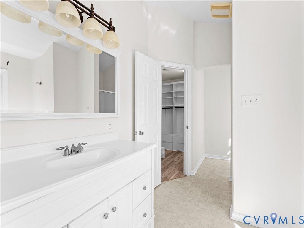 White vanity with integrated sink, brushed nickel faucet, large mirror, and overhead light fixture