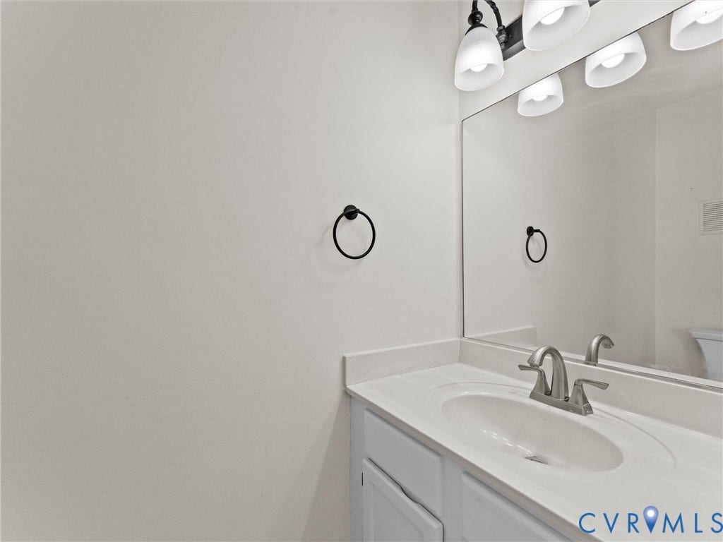 Vanity with integrated sink, brushed nickel faucet, large mirror, and overhead lighting