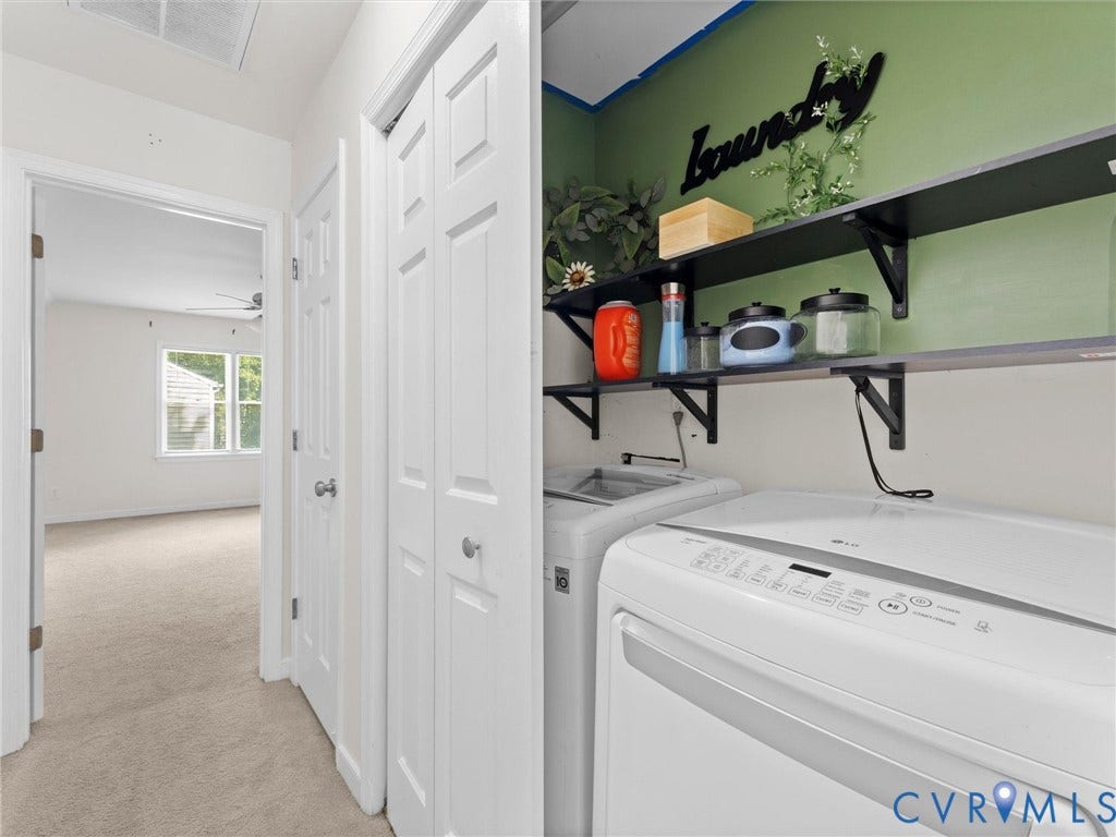 Laundry area with shelving and appliances, featuring white bi-fold doors and adjacent carpeted room with window