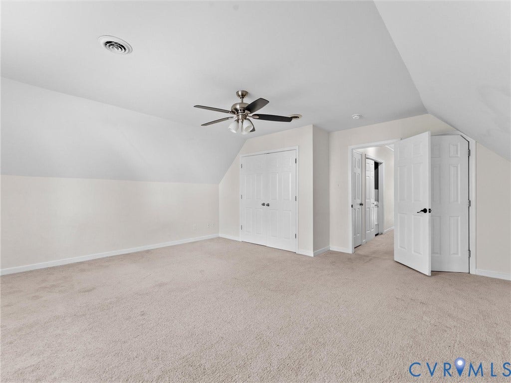Spacious room featuring sloped ceilings, neutral-toned carpeting, white panel doors, and a ceiling fan with integrated lighting