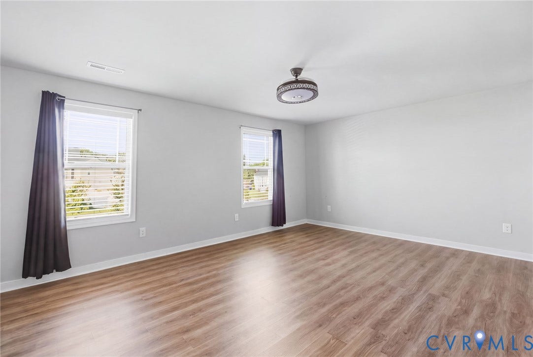 Spacious room featuring wood-finish flooring and multiple windows with blinds