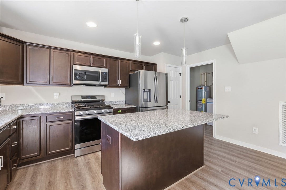 Kitchen featuring wood-finish flooring, dark wood cabinetry, light speckled countertops, and stainless steel appliances